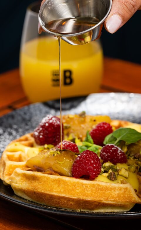 maple syrup being poured onto a plate with waffles topped with raspberries