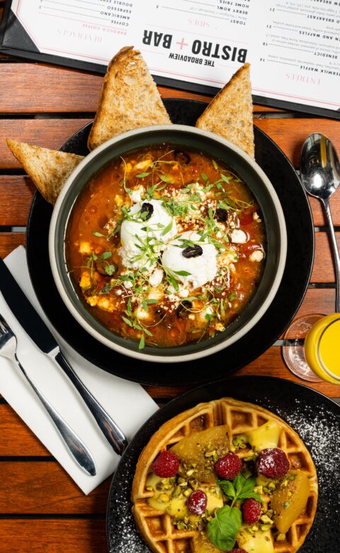 overhead shot of two black breakfast plates with shakshuka and waffles