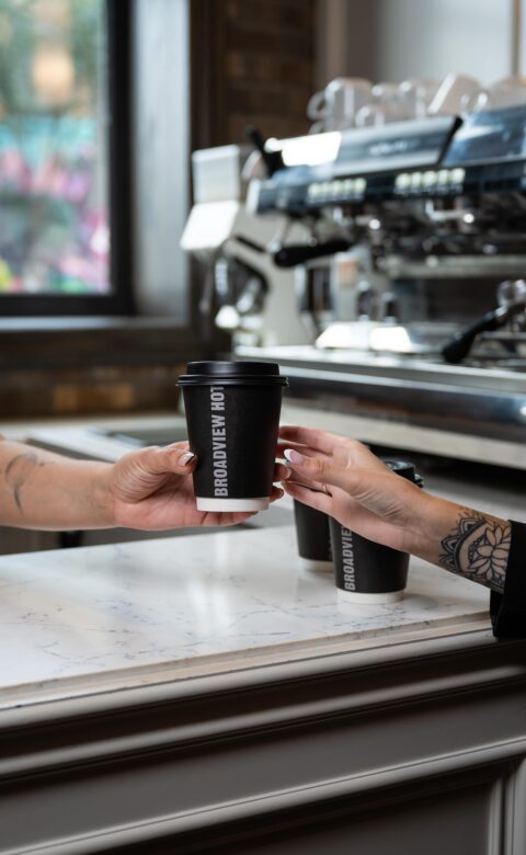 a black takeout coffee cup being handed across a takeout bar