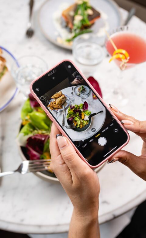 a woman holding an iphone taking a photo of her lunch salad