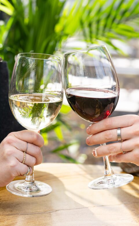 two hands holding glasses of red and white wine