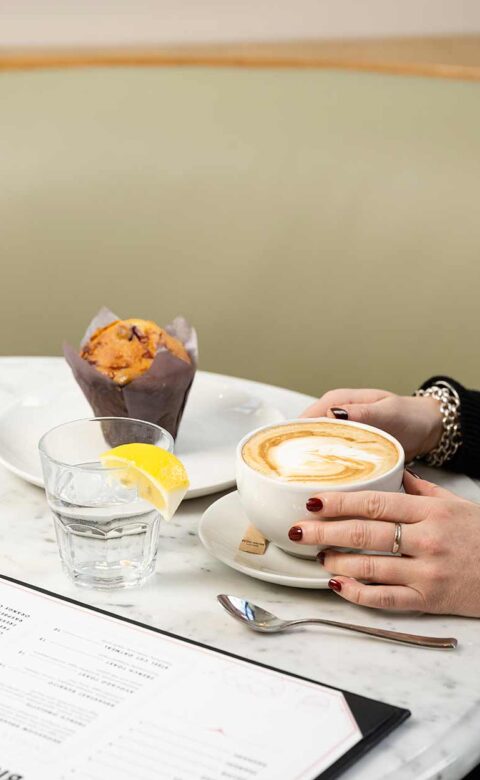 person holding coffee cup at table with glass of water and muffin