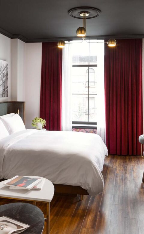 hotel room with king bed couch coffee table tv desk and large windows with red curtains