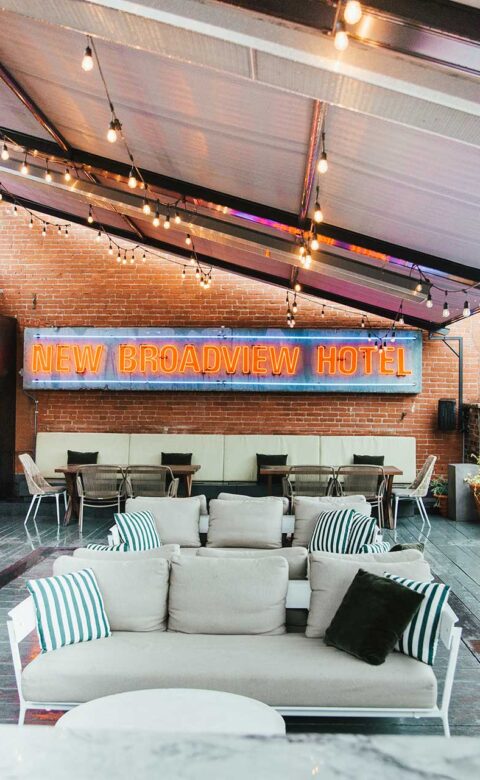 covered rooftop seating area with lit blue and orange neon new broadview hotel sign in the background