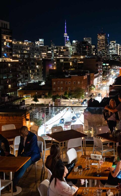 people sitting on rooftop at night with toronto skyline in the background