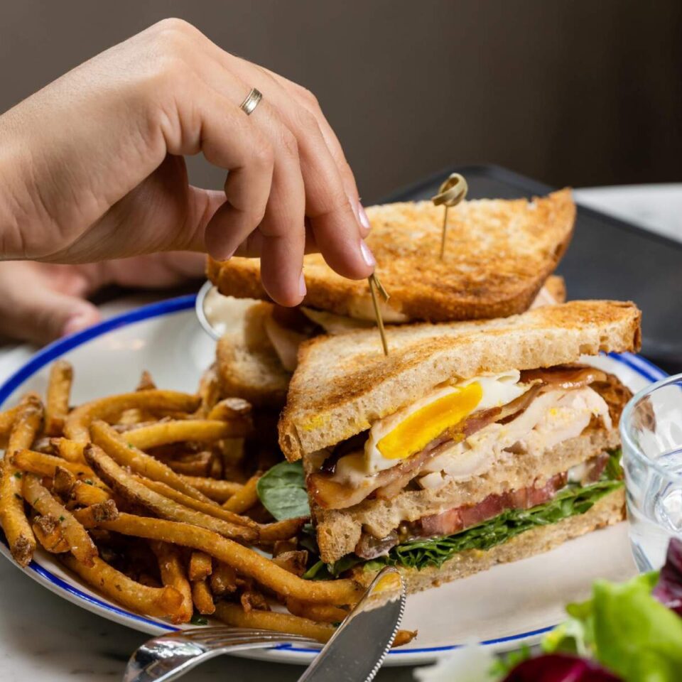 a woman eating a breakfast sandwich in a restaurant with a side of french fries