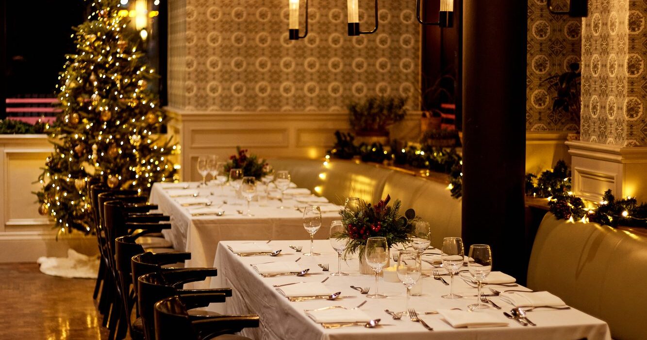 Long dining table set for an event with warm ambient lighting and holiday decor.