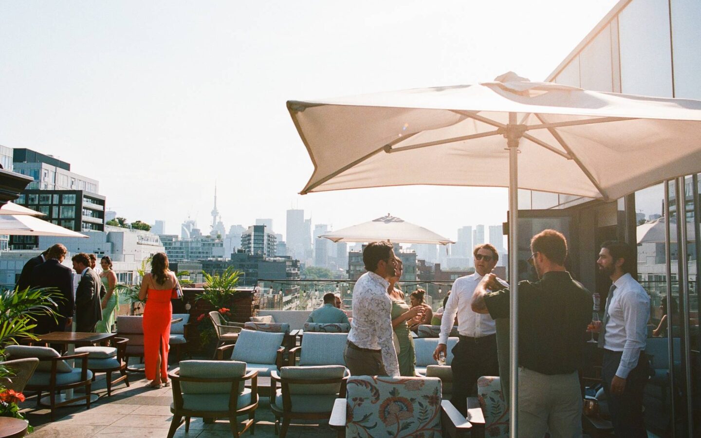 Guests mingling on a rooftop patio with umbrellas, lounge seating, and Toronto skyline views.
