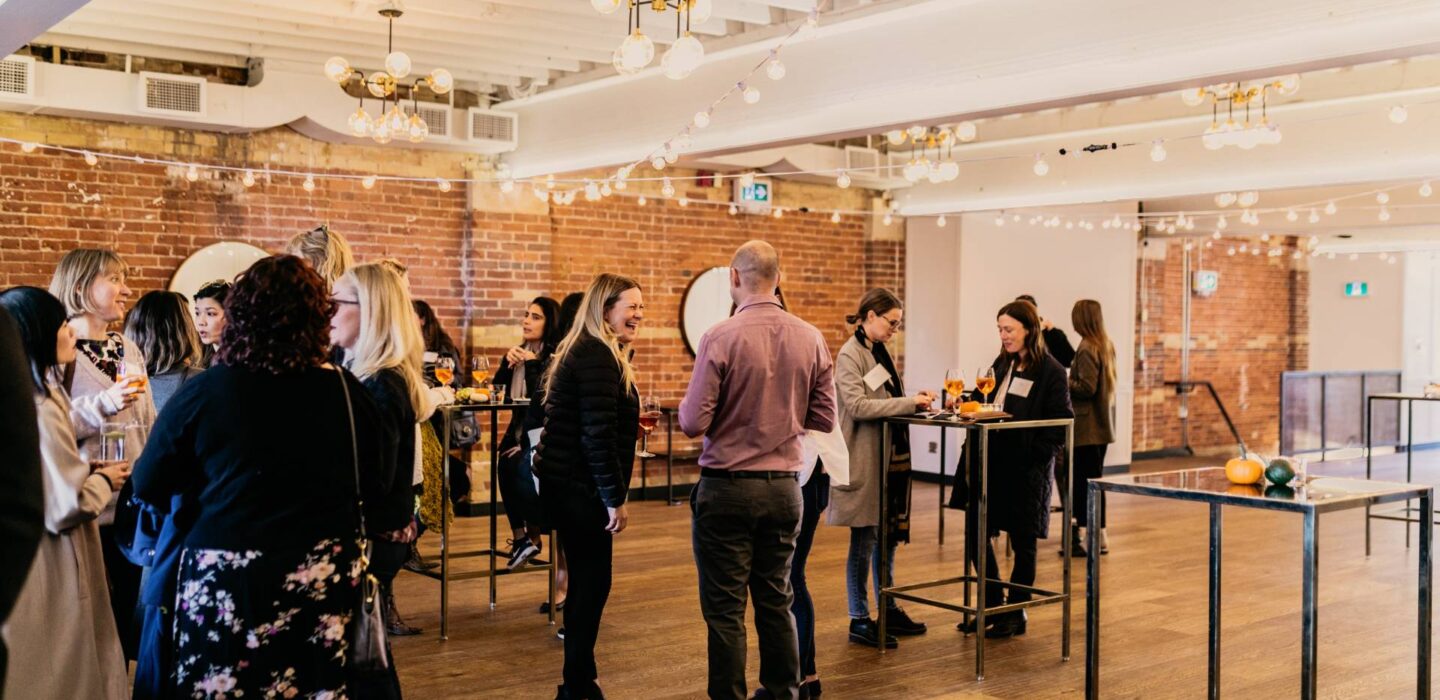 Guests mingling at a cocktail reception in Lincoln Hall with tall metal bar tables.