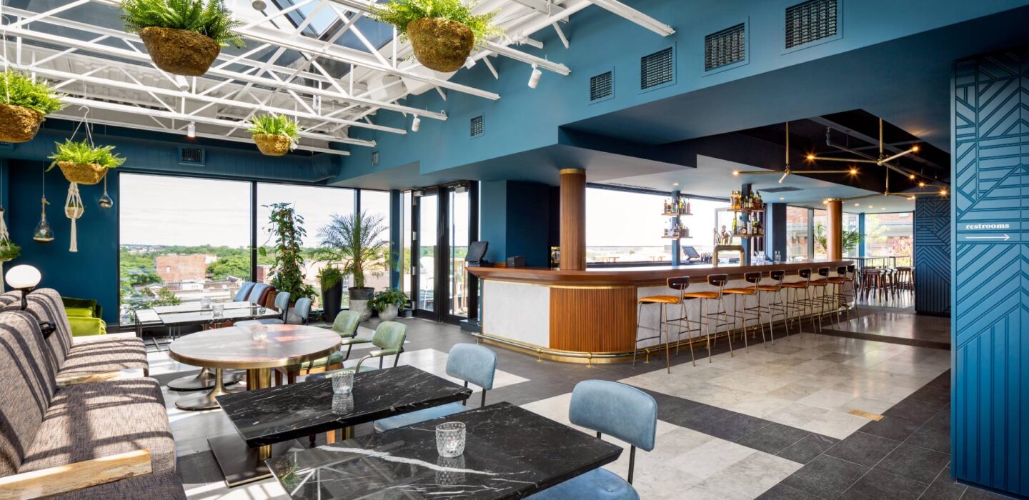 Modern rooftop seating area with a full bar counter and city skyline views through floor-to-ceiling windows.
