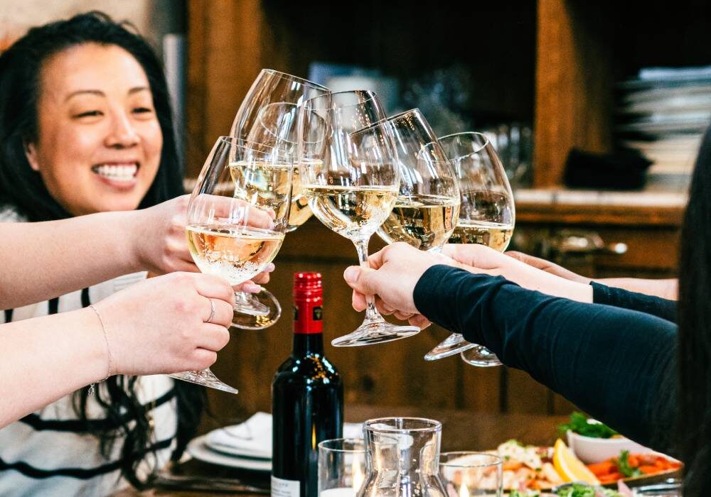 Close-up of guests toasting with white wine glasses at a private dining event.