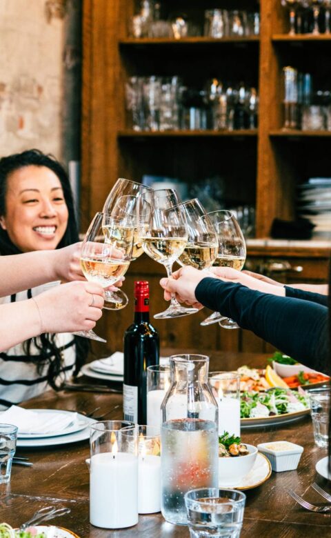 Close-up of guests toasting with white wine glasses at a private dining event.