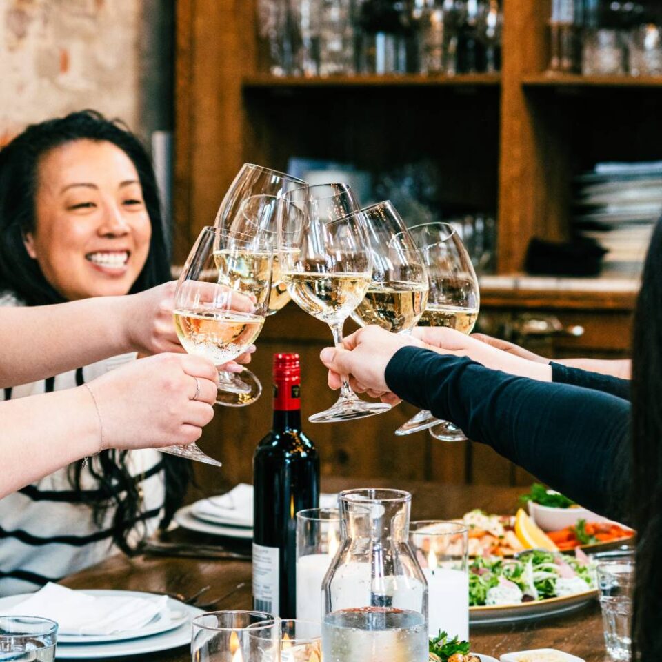 Close-up of guests toasting with white wine glasses at a private dining event.
