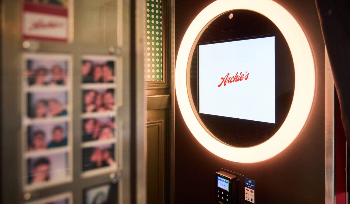 Photo booth with a glowing circular light and touchscreen, with photo strips displayed nearby.