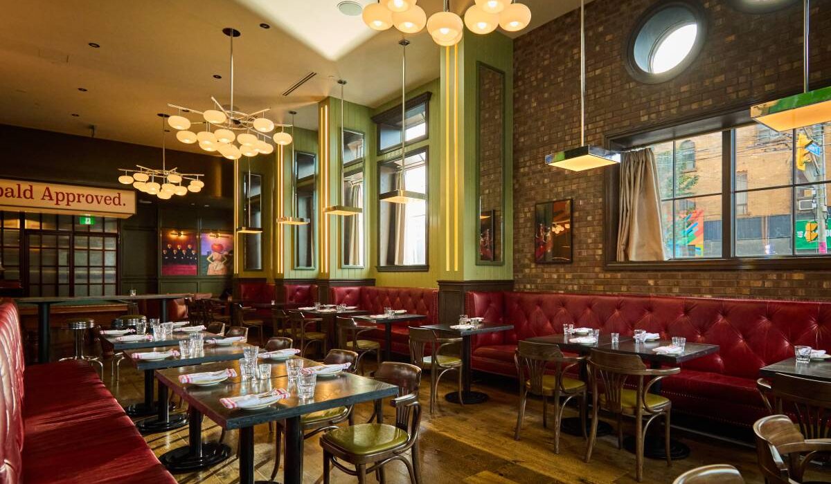 Stylish restaurant dining room with red leather banquettes, exposed brick walls, modern lighting, and neatly set tables.