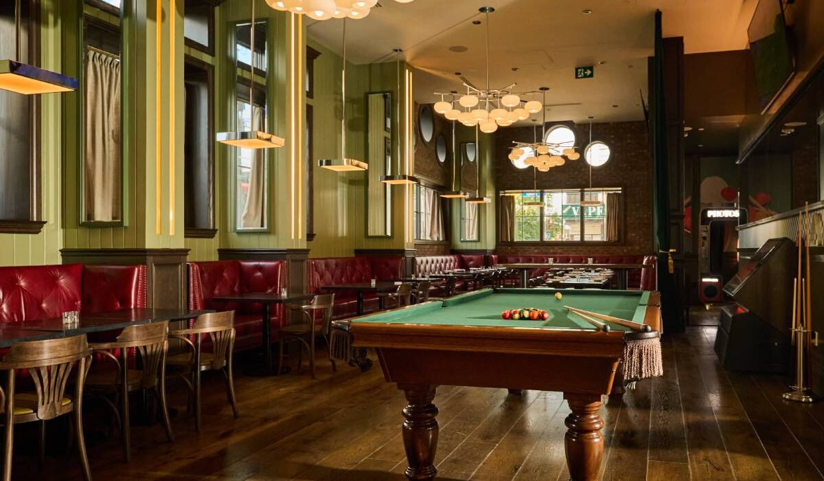 Restaurant interior with a pool table, red leather banquettes, wooden floors, and modern pendant lighting.